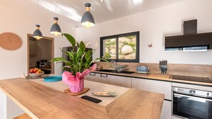 Una cocina moderna con una isla central, iluminación colgante, un amplio ventanal y horno empotrado.