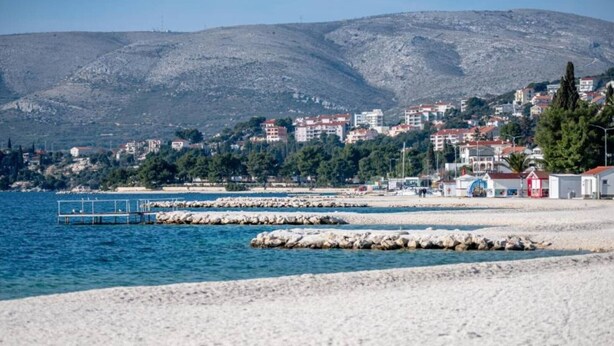 A coastal town with a sandy beach, rocky breakwaters, and buildings in the background. - One Bedroom Apartment with Balcony (Okrug Gornji)