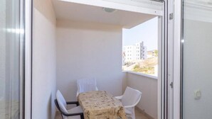 A balcony with a table and two chairs, a view of buildings, and a door. - One Bedroom Apartment with Balcony (Okrug Gornji)