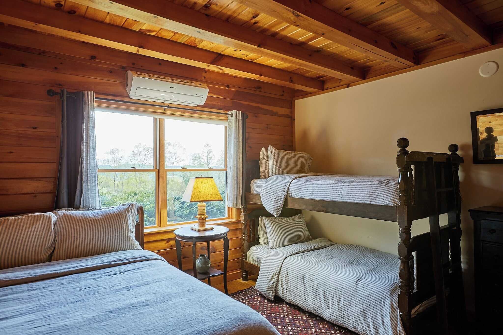 Une chambre confortable dans un chalet, avec des murs en bois, un lit superposé, un lit simple, une petite table avec une lampe et une fenêtre avec des rideaux.