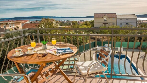 A balcony with a wooden table, two chairs, a magazine, and a glass of orange juice. - Four Bedroom Holiday Home with Pool (Kastel Stari)