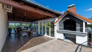 An outdoor patio with a barbecue area, a dining table with chairs, and a covered seating area with a view of the garden. - Four Bedroom Holiday Home with Pool (Kastel Stari)