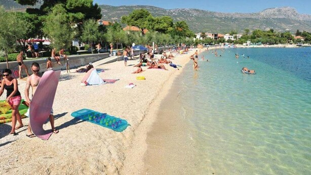 Une plage à l’eau claire, où l’on peut voir des gens se prélasser au soleil, et quelques parasols.