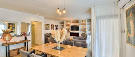 A modern living room with a wooden dining table, grey sofas, and a fireplace.