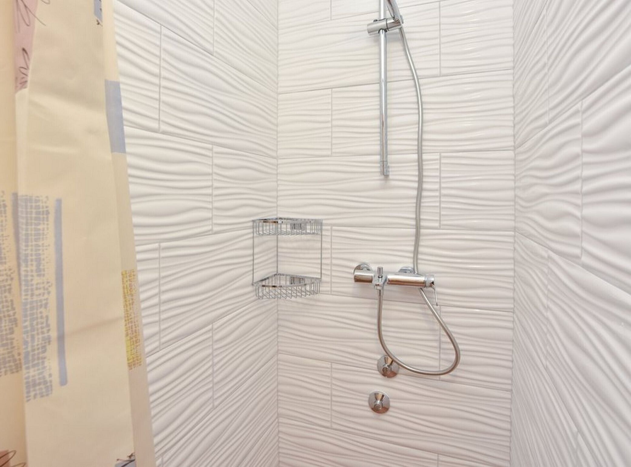 A shower area with a metal showerhead and hose, a metal shelf, and a textured wall.