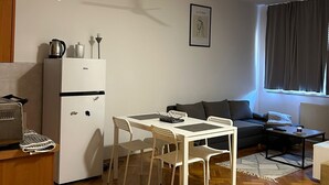 Ein kompakter Wohnbereich mit Küchenzeile, einer Essecke mit Tisch und Stühlen, einer Sitzecke mit Sofa und einem Deckenventilator.