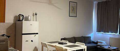 A compact living space with a kitchenette, a dining area with a table and chairs, a sofa, and a ceiling fan.
