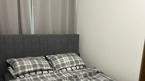 Ein Bett mit grauem Kopfteil und einer grau-weißen karierten Tagesdecke.