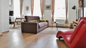 A modern living room with a brown sofa, a red chair, and a dining area with a table and chairs.