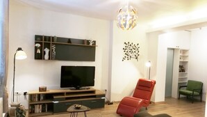 A modern living room with a flat-screen TV, a red chair, a green chair, and a decorative wall piece.