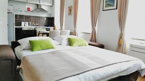 A hotel room with a bed, a desk, a chair, a kitchenette, and a window with curtains.