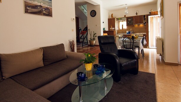 A living room with a sofa, a glass coffee table, and a dining area with a table and chairs. There is a kitchen in the background with cabinets and a refrigerator. - Four Bedroom Holiday Home (Rijeka)