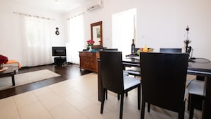 A modern living room with a dining area, featuring a flat-screen TV, wooden furniture, and a large mirror.