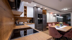 Une cuisine moderne dotée d’un îlot central, d’un four encastré et d’un coin repas avec des chaises roses.