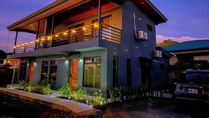 A modern two-story house with a balcony, outdoor lighting, and a vehicle parked in front. - Monstera Apartments Monteverde (Monteverde)