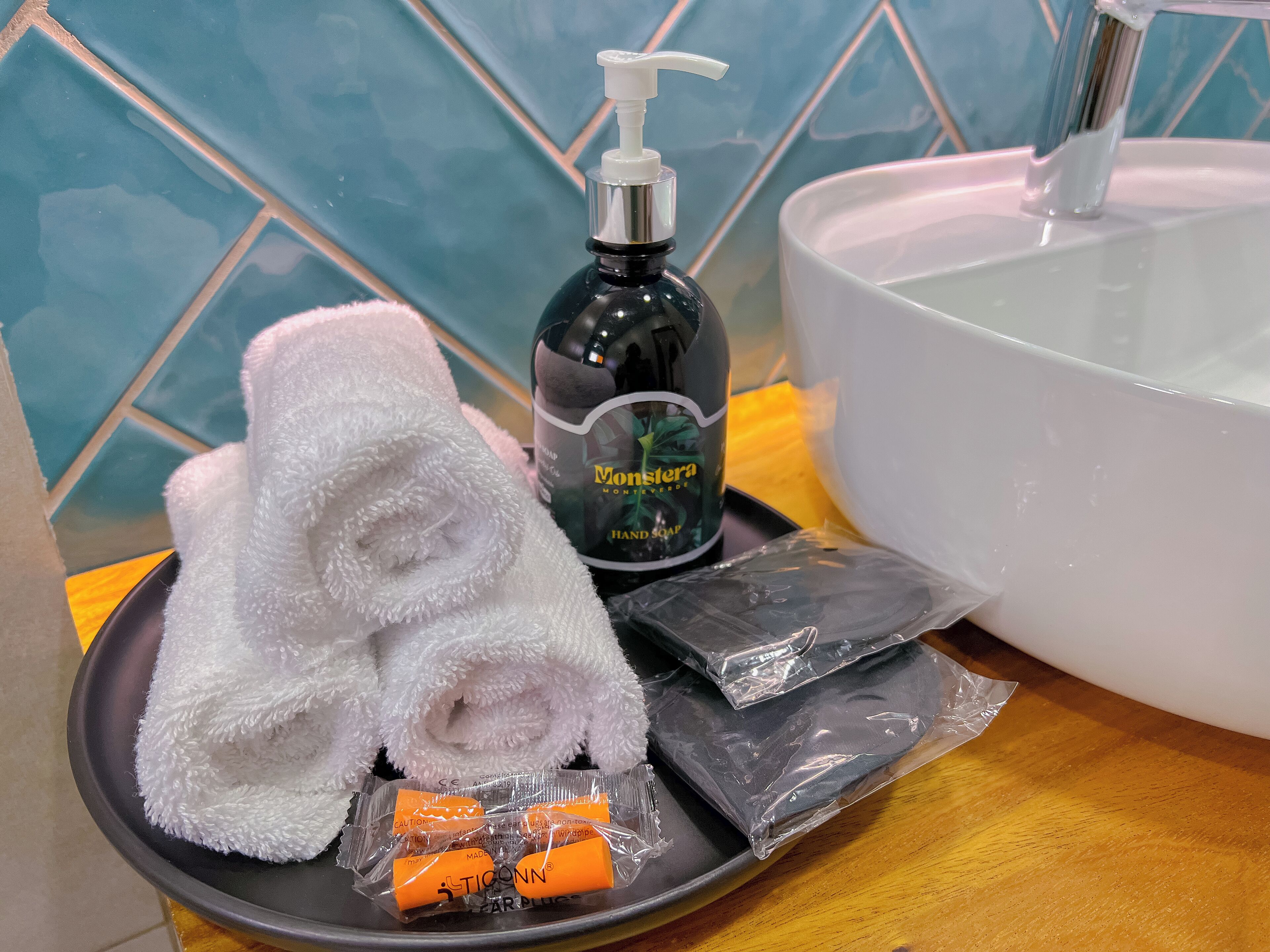 A bathroom with a white sink, a bottle of hand soap, a white towel, and a tray with toiletries.