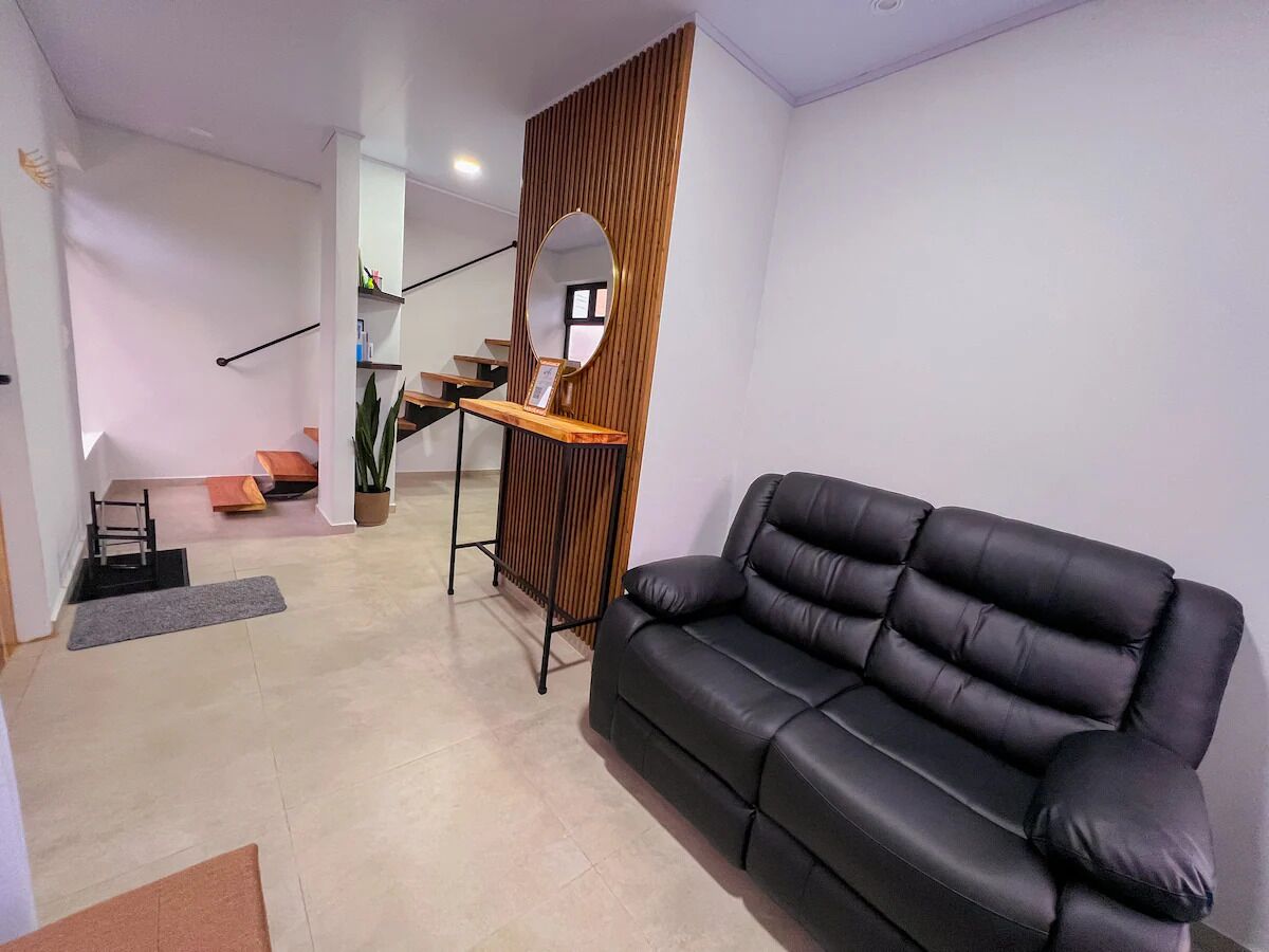 A modern living room with a black leather sofa, a wooden sideboard, and a mirror.