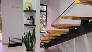 A modern staircase with wooden steps and a black handrail, leading to a landing with a bookshelf and a potted plant. - Monstera Apartments Monteverde (Monteverde)