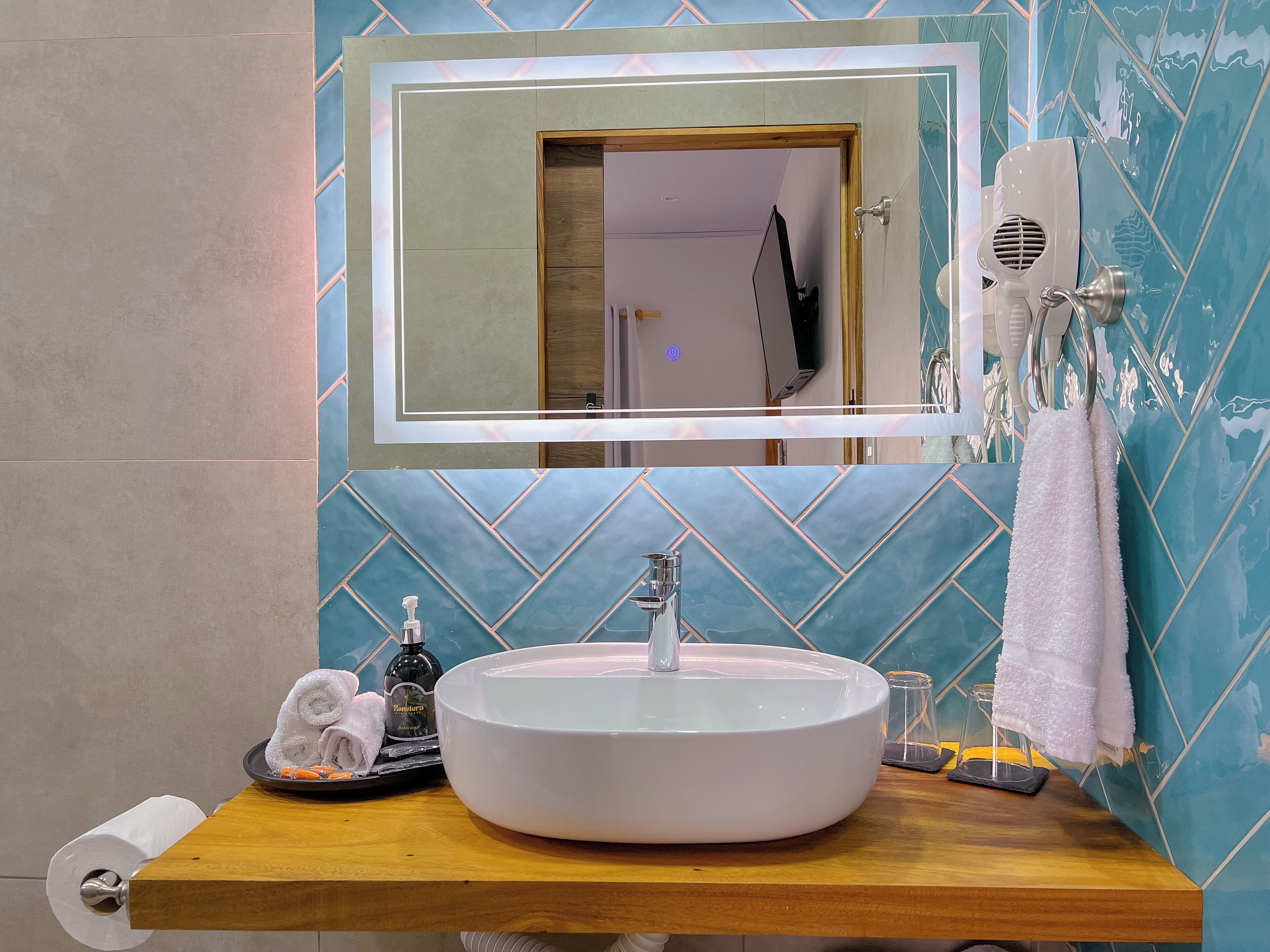 Un baño con lavamanos redondo, un espejo, un perchero para toallas y un secador de pelo.