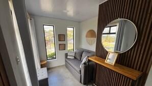 A modern living room with a grey sofa, a wooden console table, and a large mirror. There are two windows providing a view of the outside. - Monstera Apartments Monteverde (Monteverde)