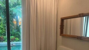 A room with a beige sofa, a large mirror, and a view of a swimming pool and greenery outside. - Charming Ocean line studio with largest pool in beautiful Troncones (Troncones)