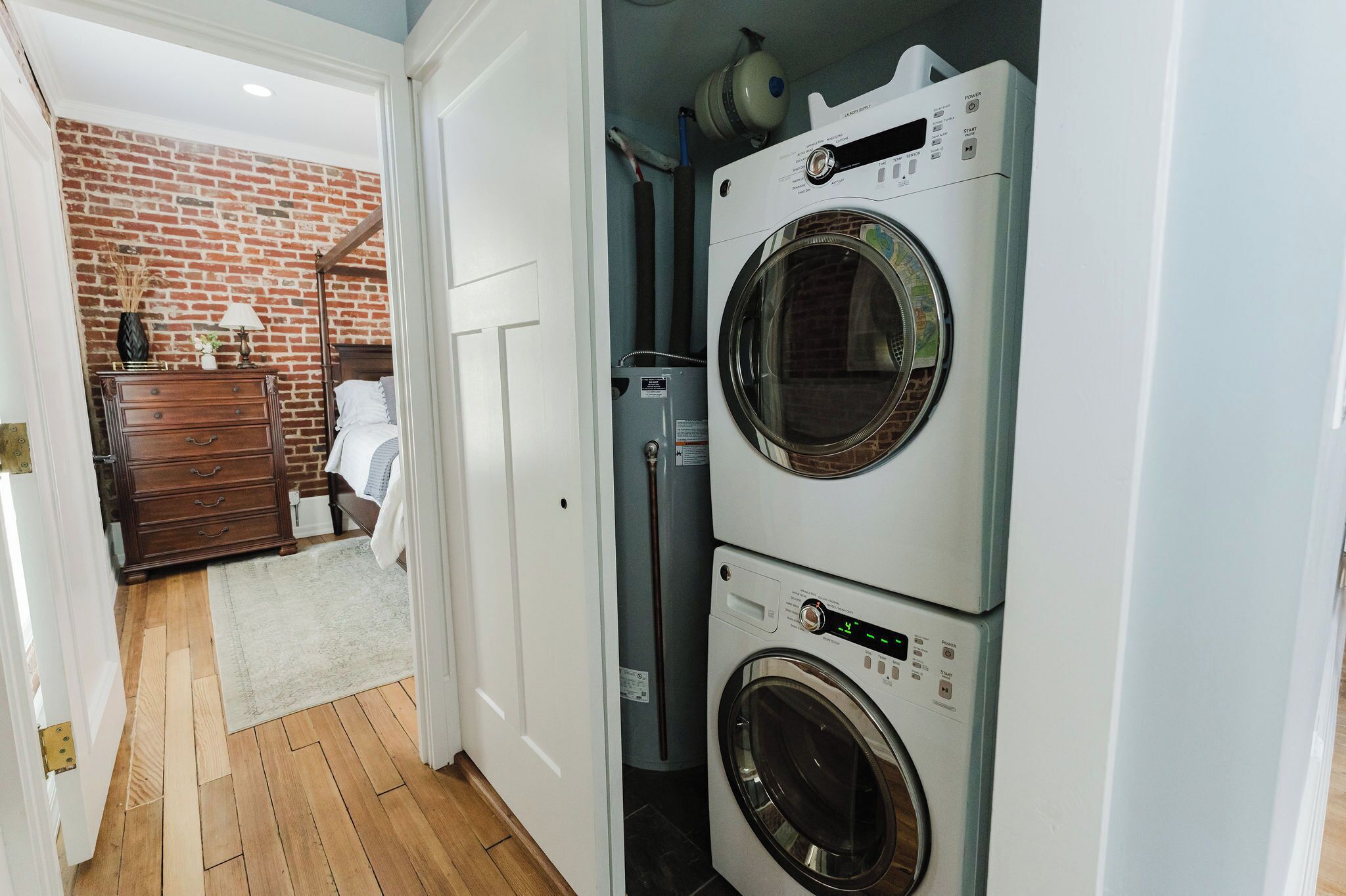 Une buanderie avec des lave-linge et des sèche-linge superposés, une commode en bois et un mur décoré d’un motif en briques.