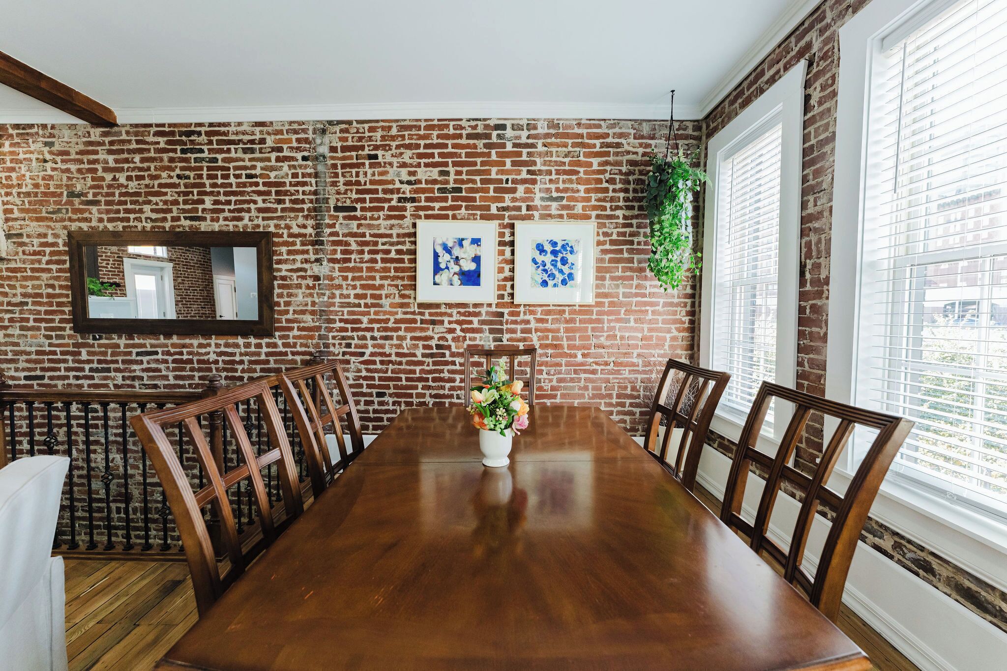 Uma sala de jantar com parede de tijolos, mesa de madeira, cadeiras e um vaso de flores.