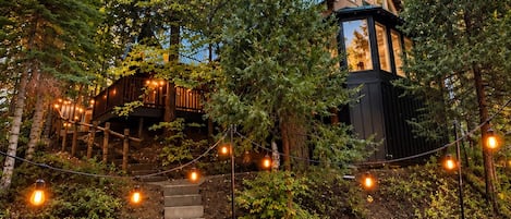 A cabin with a deck, surrounded by trees, and outdoor seating with a fire pit.