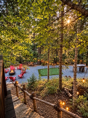 An outdoor seating area with red chairs and a fire pit, surrounded by trees and string lights.