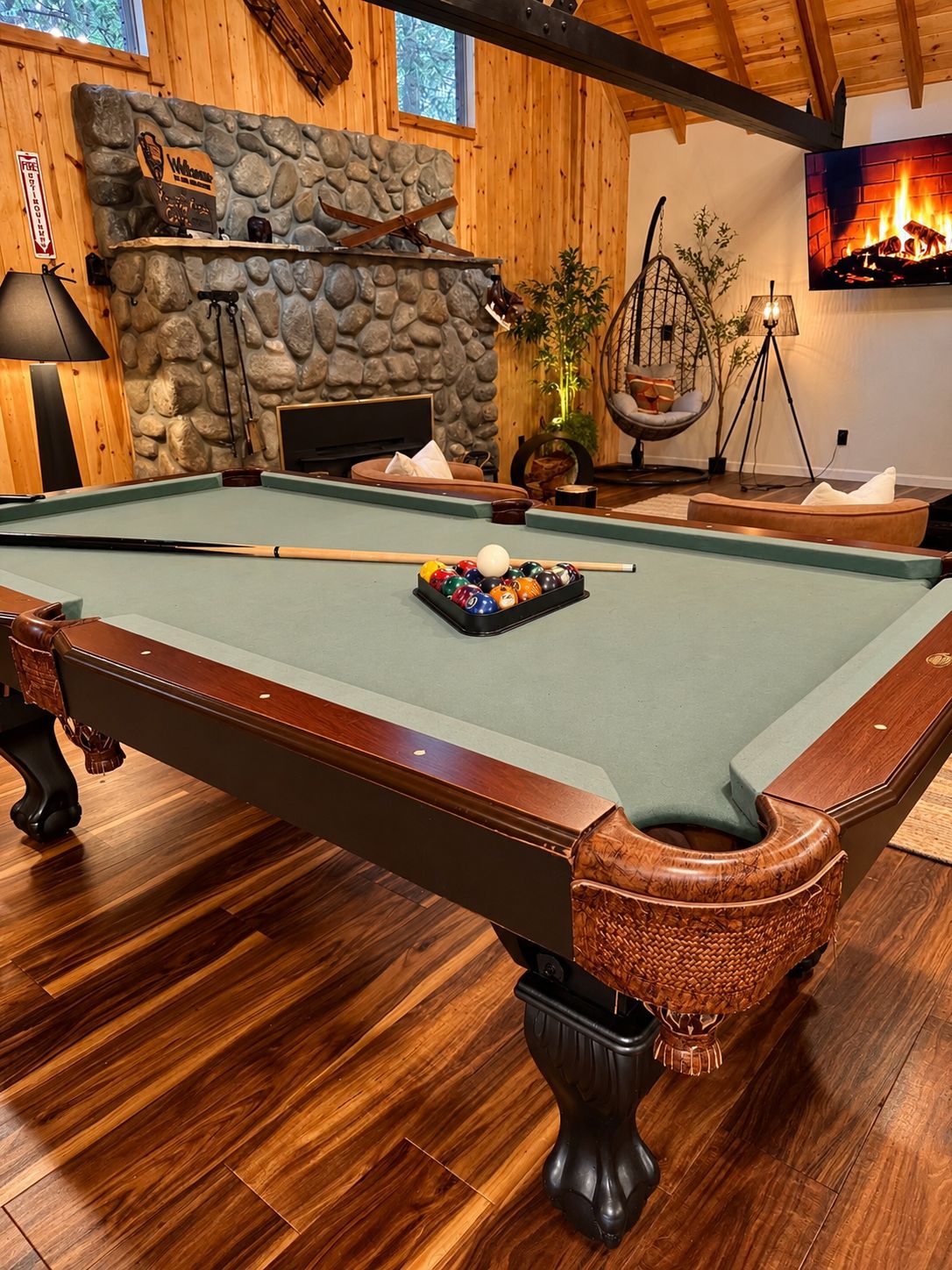 Een pooltafel met een stenen openhaard, houten wanden en een hangstoel.