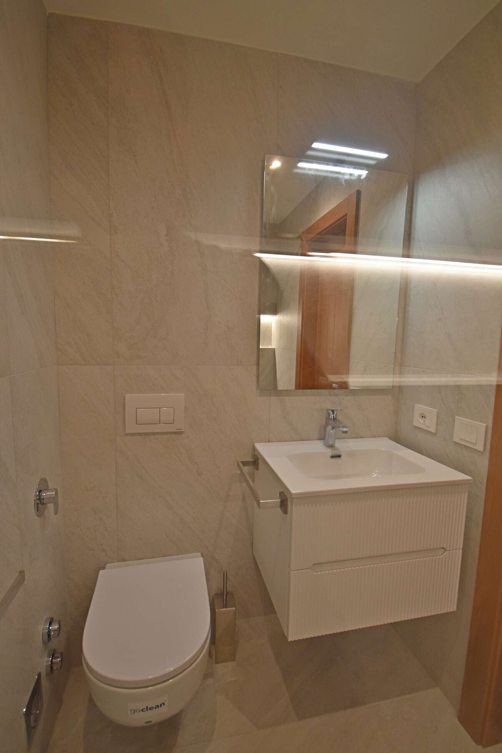 A bathroom with a toilet, sink, mirror, and towel rack.