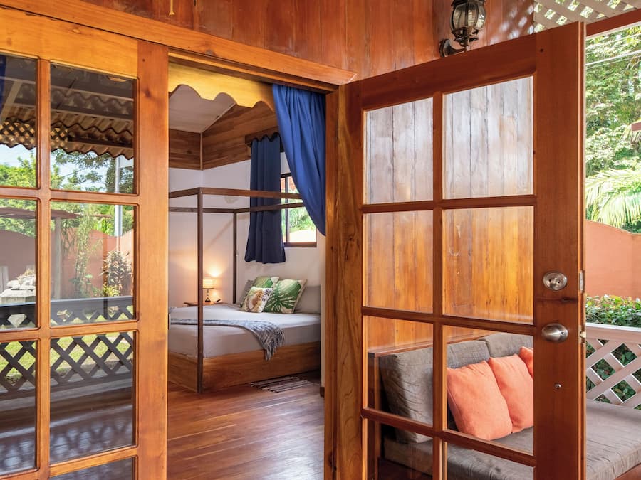 A wooden room with a bed, a bench, and a view through a glass door.