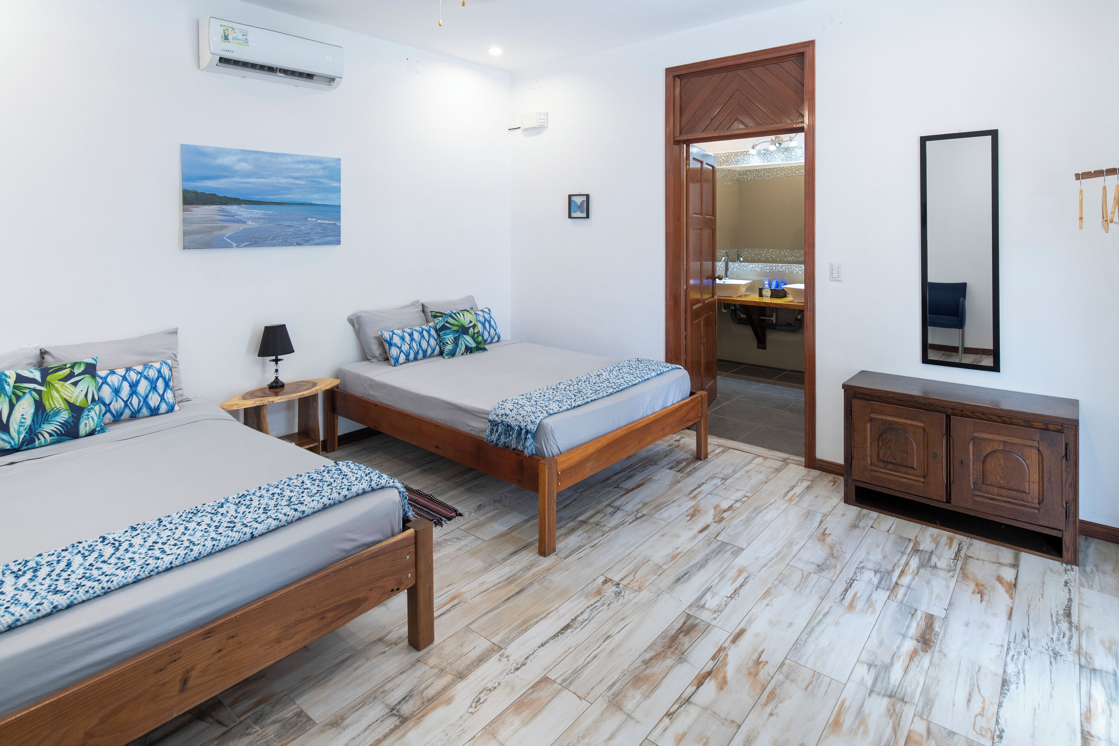 A bedroom with two beds, a wooden cabinet, a mirror, and a painting on the wall.