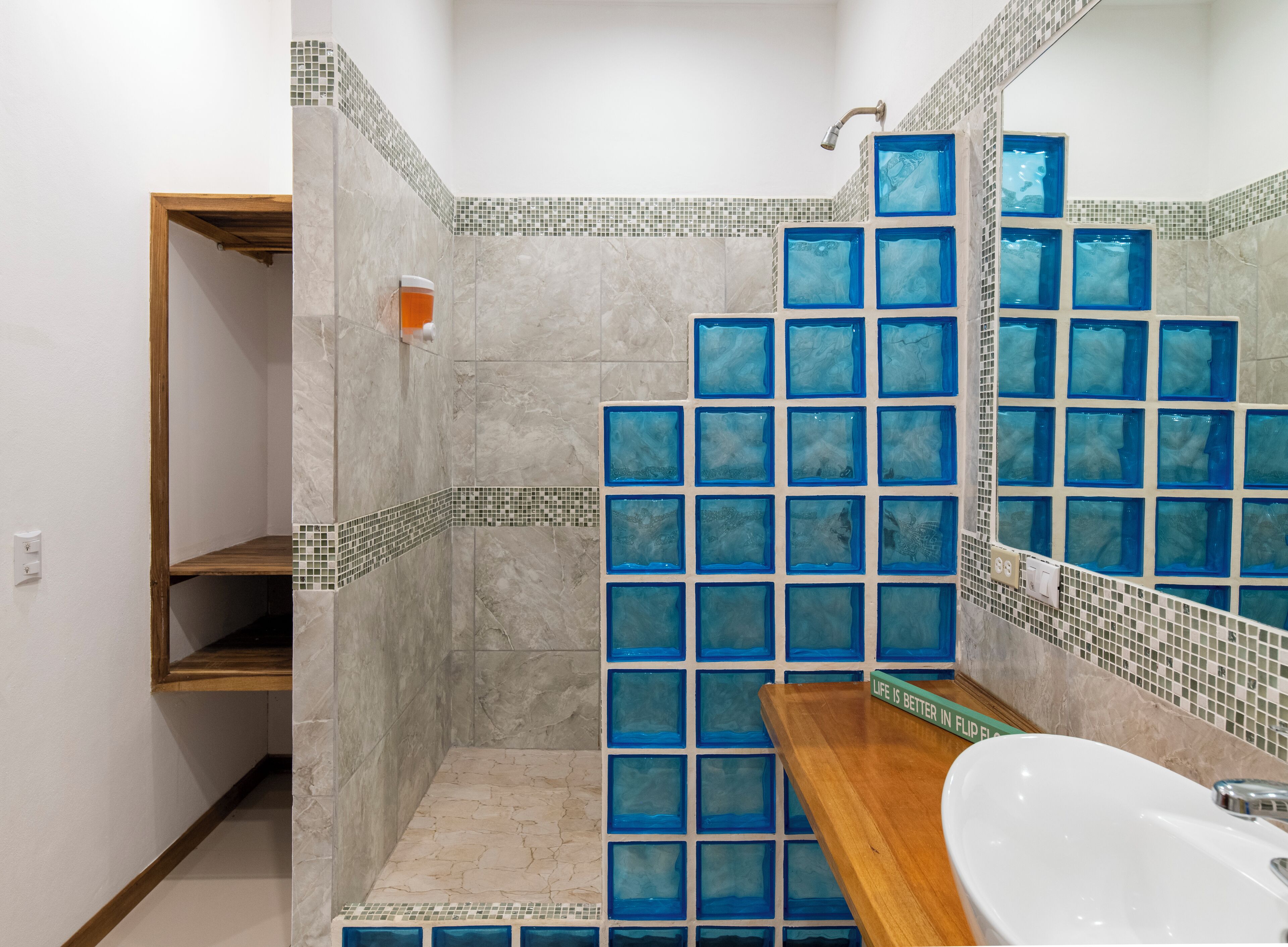Une salle de bain avec une douche, une étagère en bois et un lavabo.