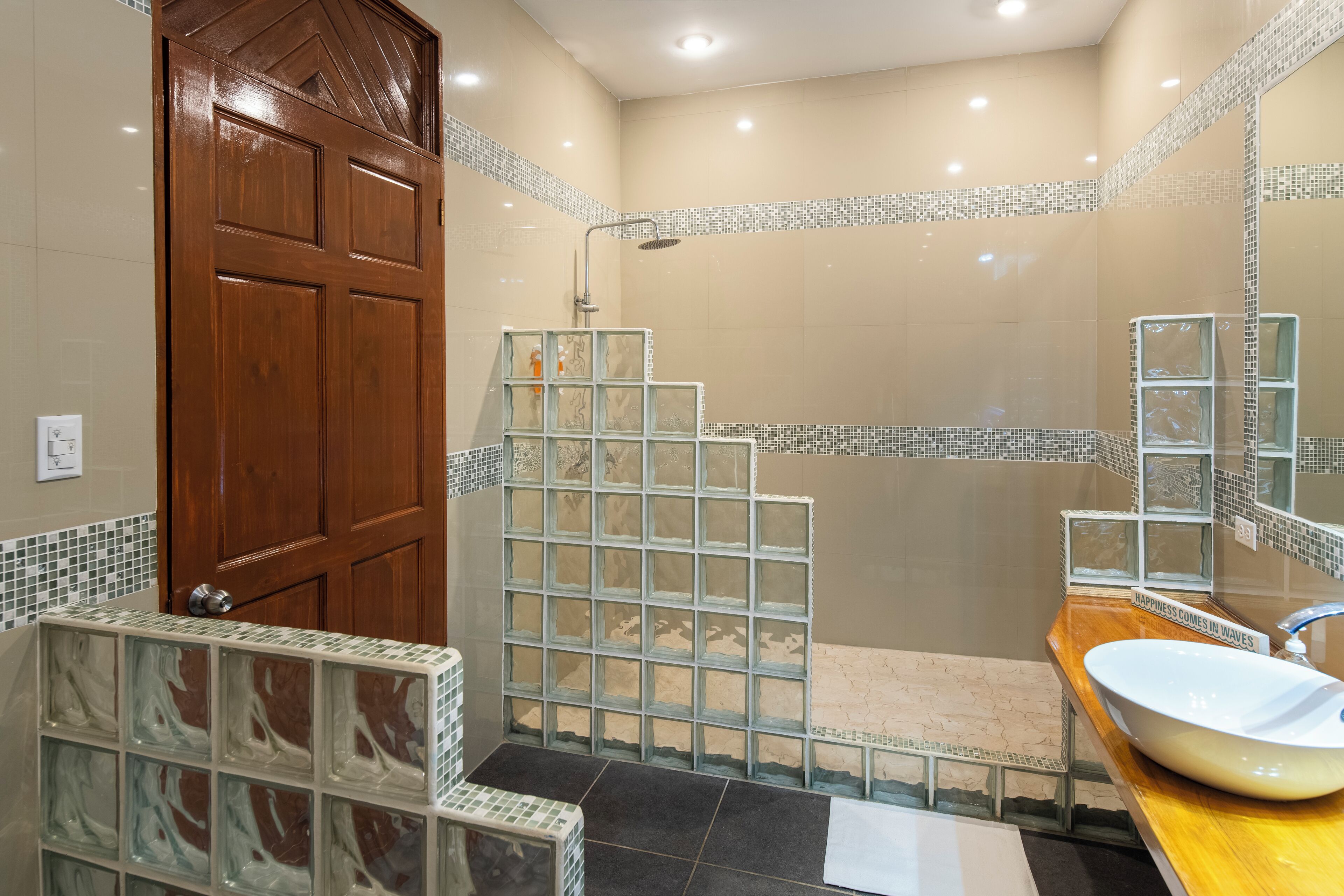 A bathroom with a wooden door, a glass shower enclosure, a sink with a mirror, and tiled walls.