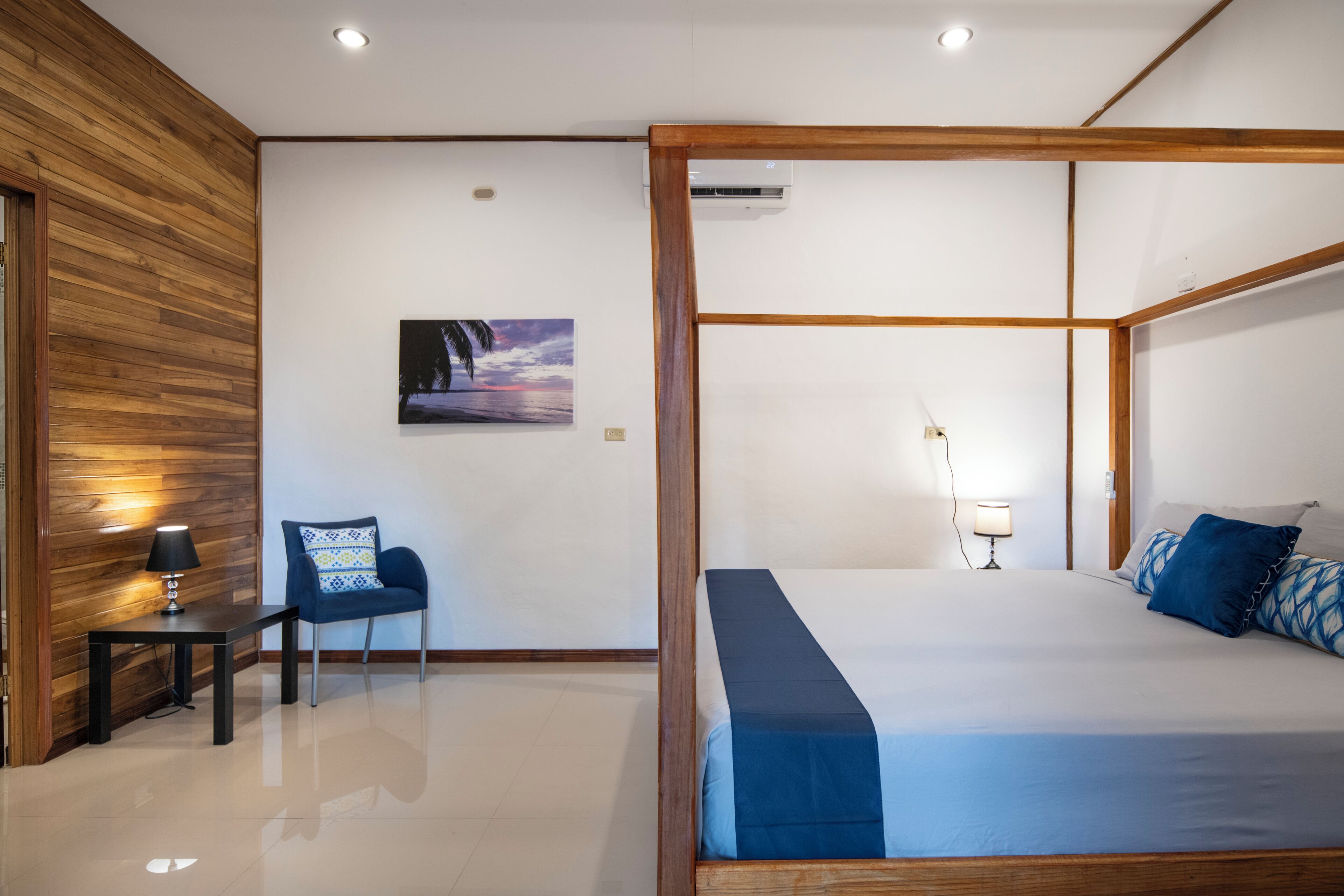 Un dormitorio con una cama con dosel, una silla, una mesita pequeña y un aire acondicionado de pared.