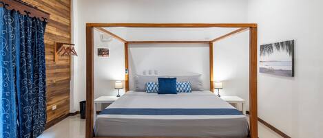 Un lit à baldaquin avec une structure en bois, une literie blanche et un plaid bleu. Il y a deux tables de chevet avec des lampes, un panneau mural en bois et un tableau encadré accroché au mur.