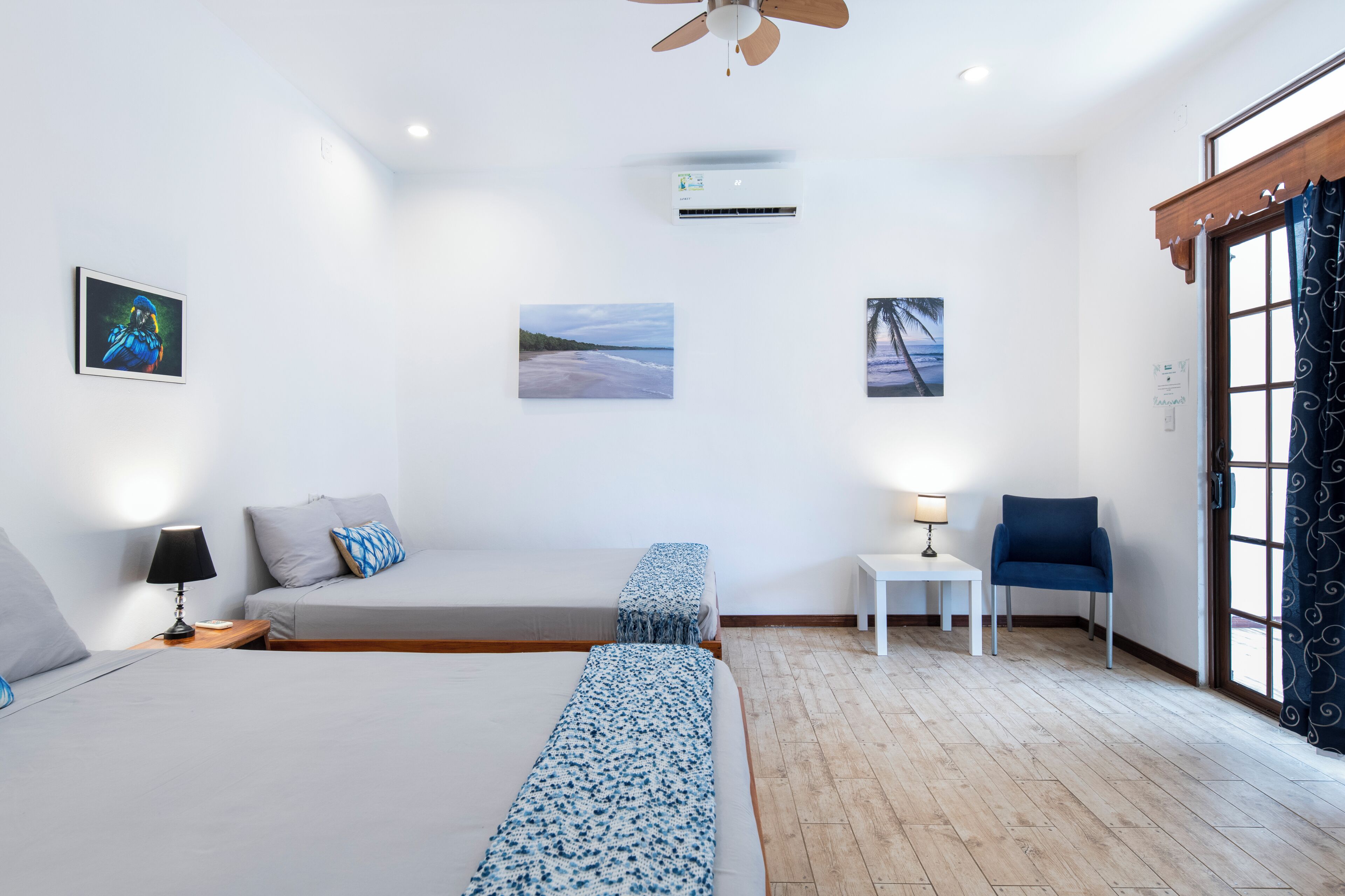 Een hotelkamer met een groot bed, een slaapbank, een tafeltje met een lamp, een stoel en een raam met gordijnen.