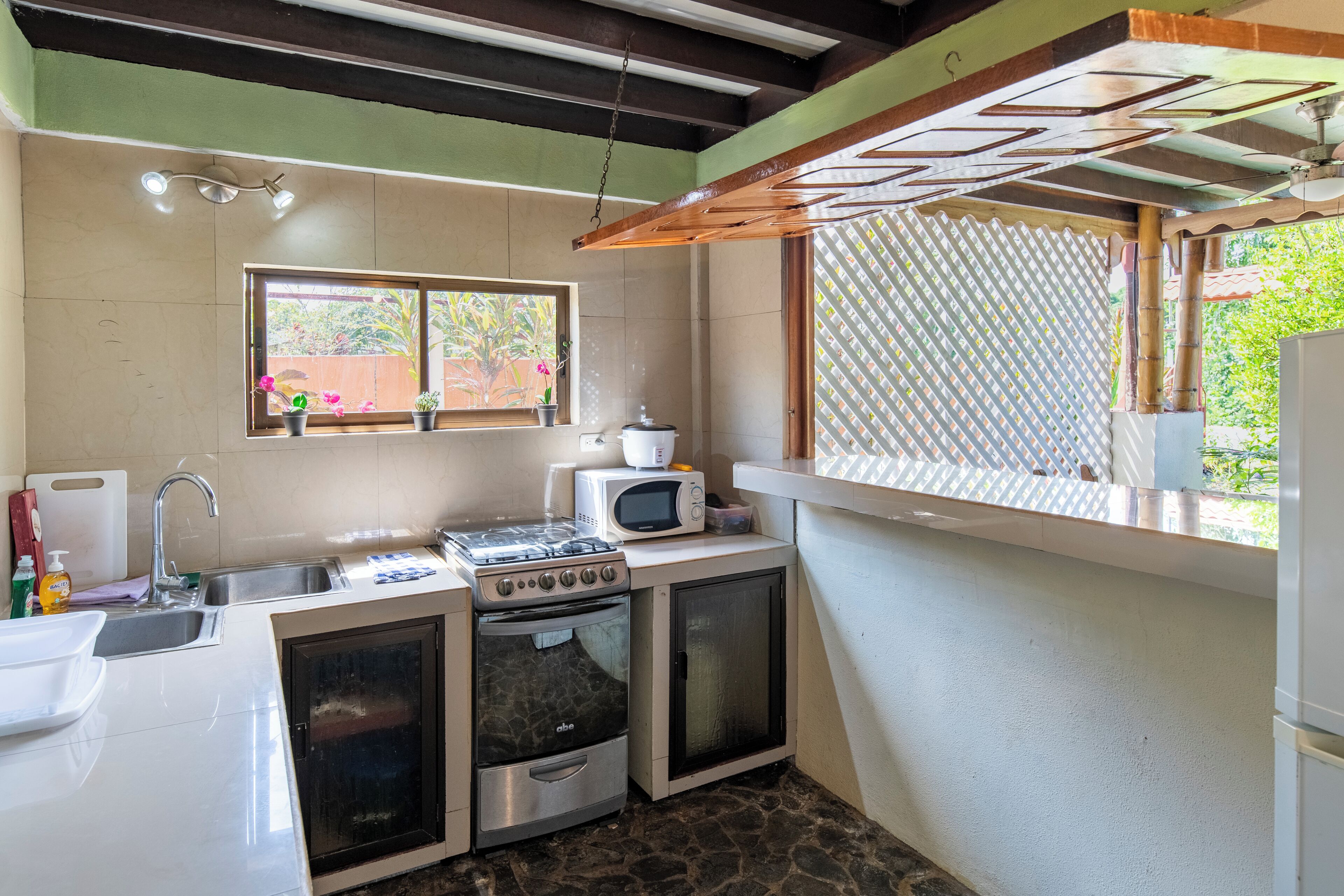 A compact kitchen with a stove, microwave, and oven. There is a window with a view of greenery outside.
