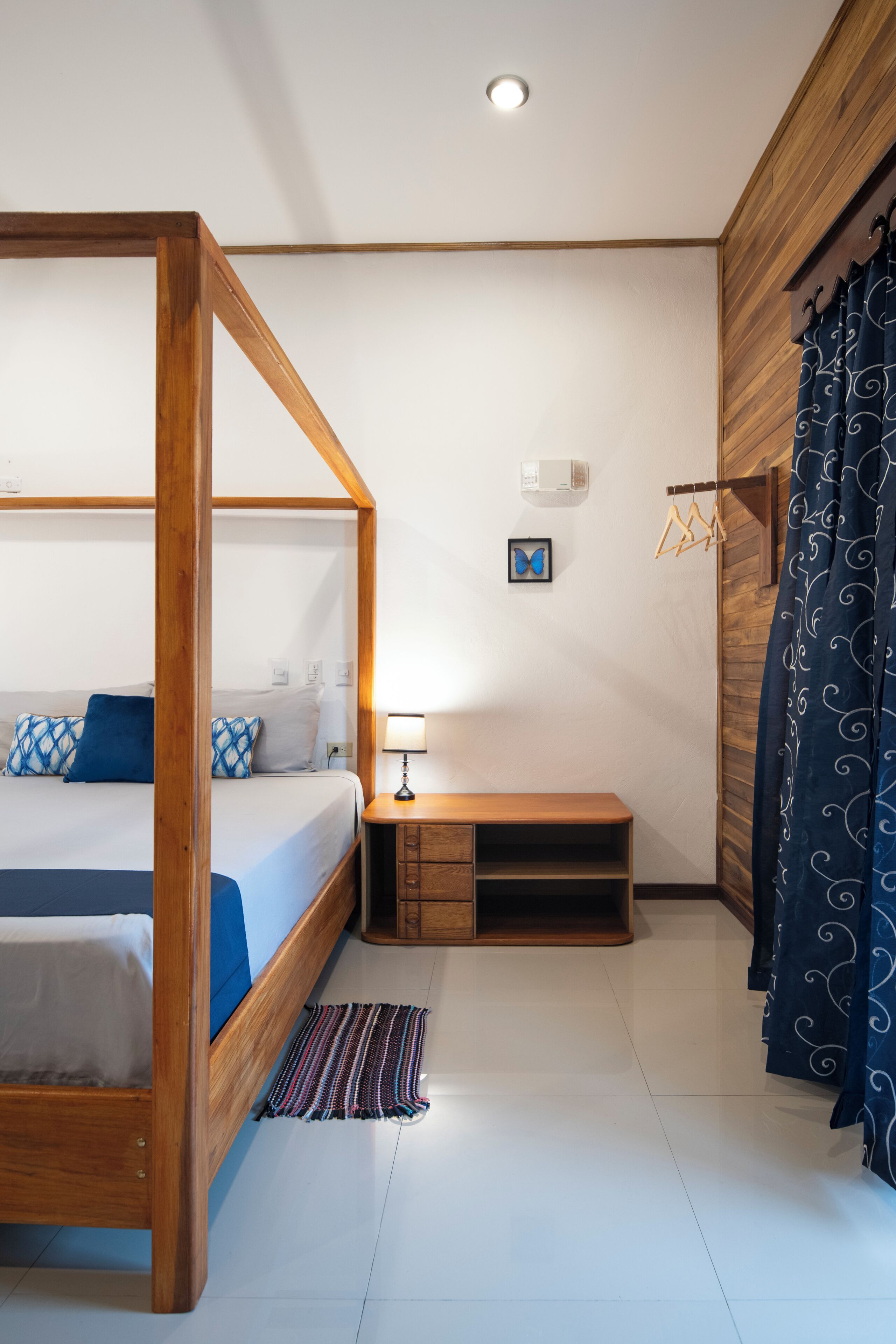 Ein Schlafzimmer mit Himmelbett, Nachttisch mit Lampe, kleiner Holzbank und Wandklimaanlage.