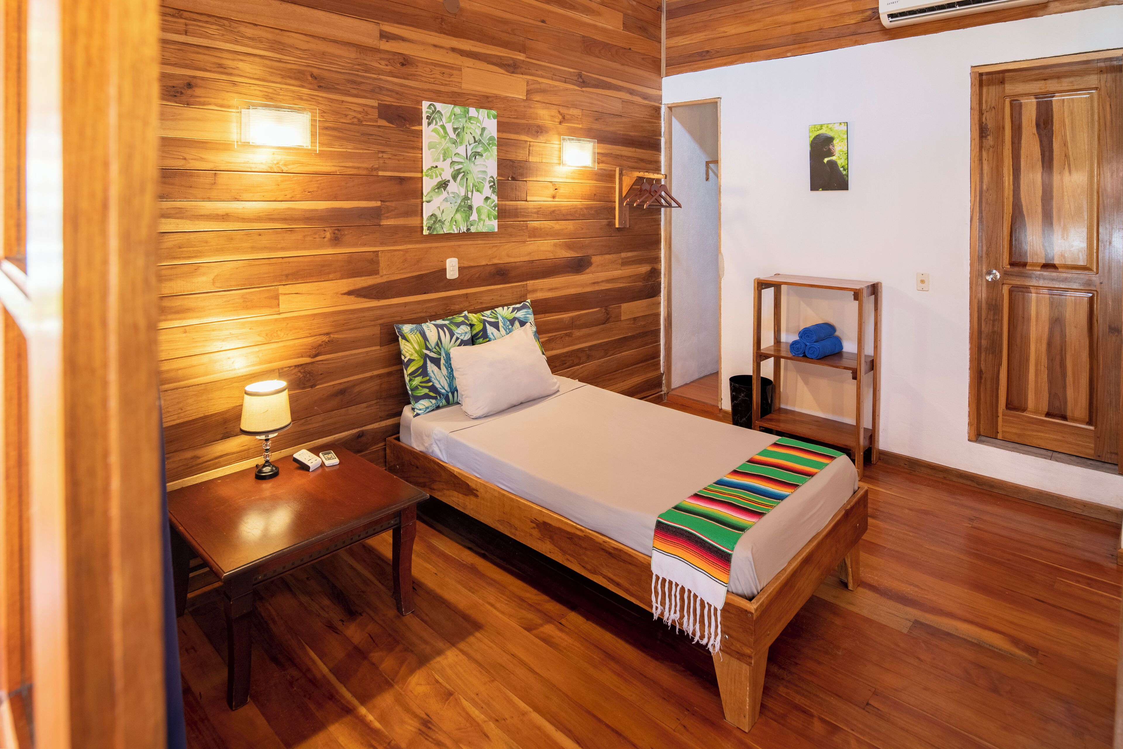 A wooden-paneled room with a bed, bedside table, lamp, and wall-mounted light fixture.