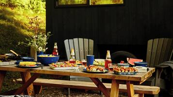 A wooden cabin with a dining table set for a meal, surrounded by chairs, and a bench with a blanket.