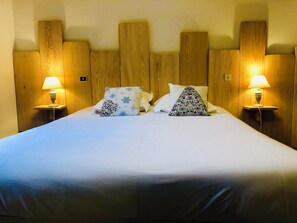 Una cama bien tendida con dos almohadas, una mesita de noche con lámpara y paneles de cabecera de madera.