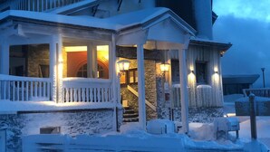 Una casa cubierta de nieve con un porche, paredes de piedra y una escalera que lleva a la entrada.