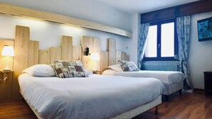 Un dormitorio con dos camas, cabeceros de madera, lámparas de noche, un ventanal con cortinas y un radiador.