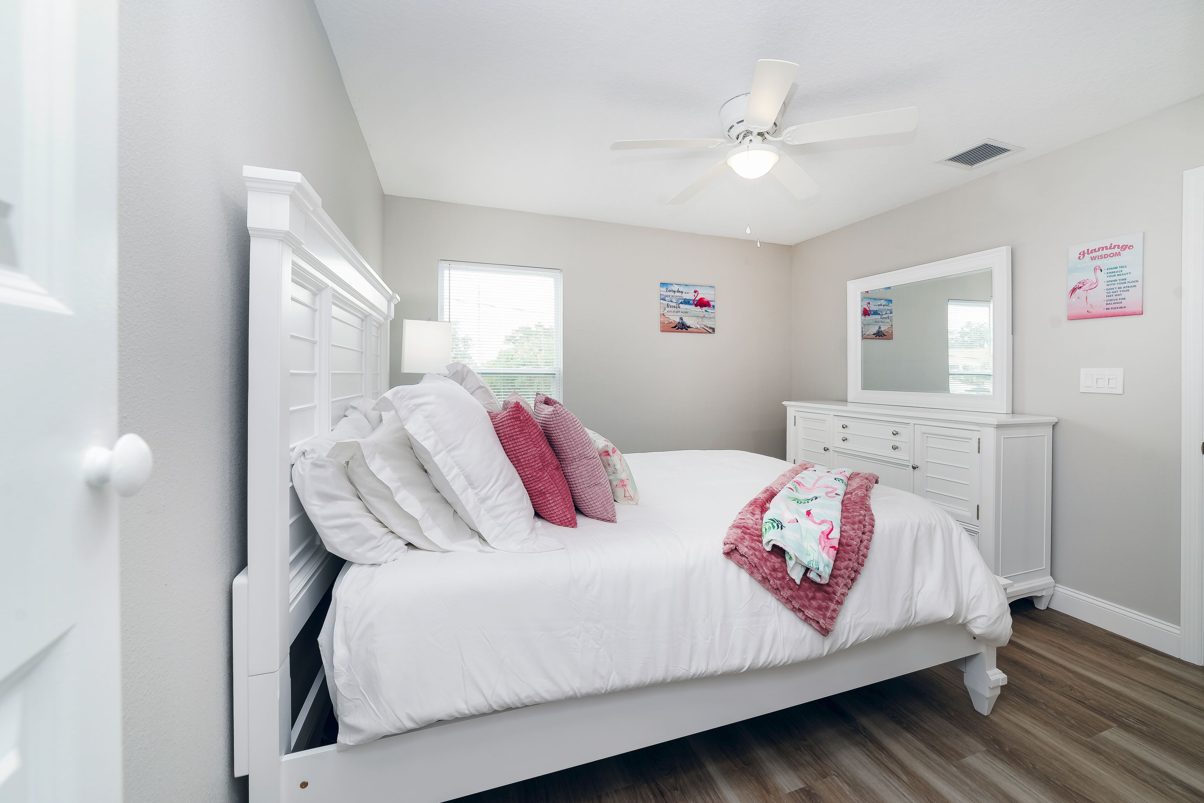 A bedroom with a white bed, a white dresser, a ceiling fan, and a window.