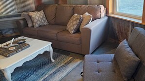 A living room with a brown sofa, a white coffee table, and a patterned rug. - Foxy's Den cozy grain bin cabin with WiFi & AC in serene Kidder. Quiet & serene. (Kidder)