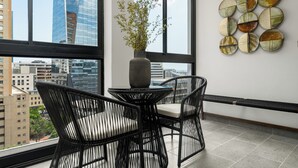 Una habitación moderna con un ventanal grande, una mesa redonda con sillas, un jarrón con plantas y una obra de arte en la pared.