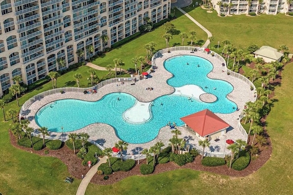A hotel with multiple swimming pools, a covered area, and a large building in the background.