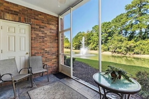 A room with a brick wall, a door, a glass door leading outside, a small table with a plant, and two chairs.